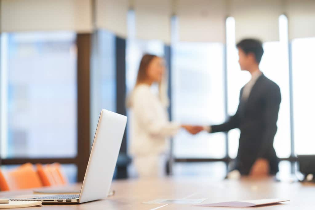 close up on laptop with blurred businesspeople hand shake together for success meeting concept