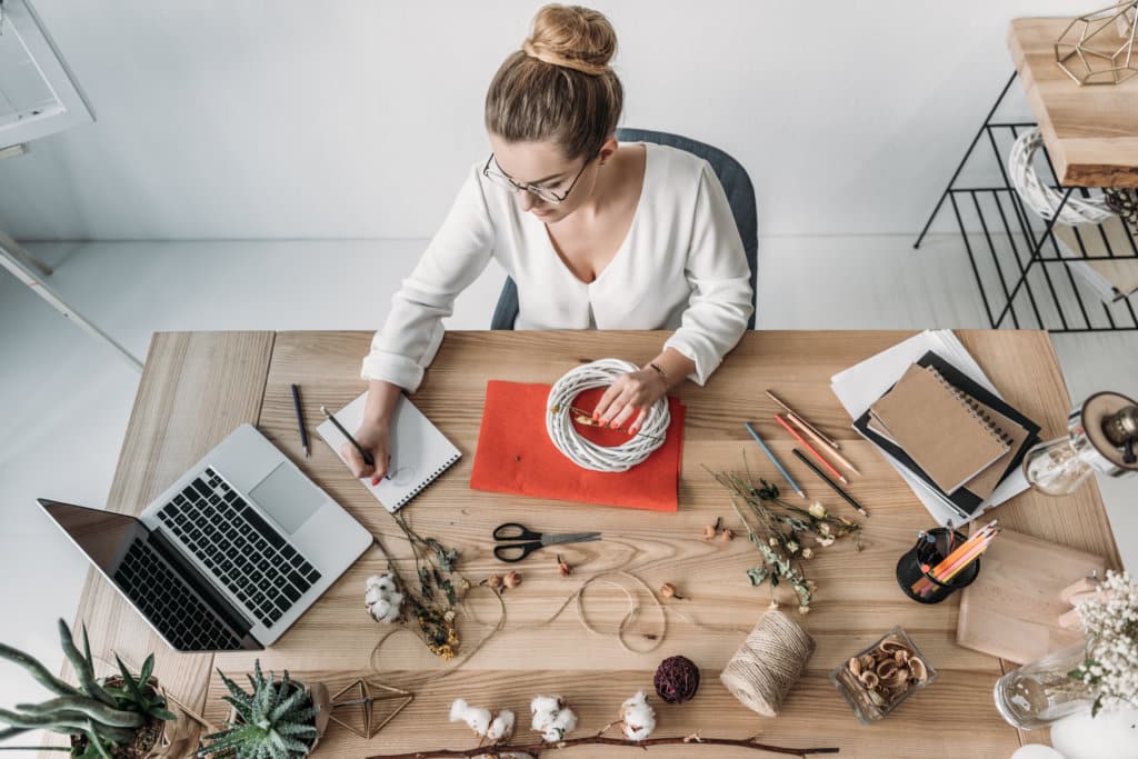 top view of blonde female florist working with laptop and dry flowers at workplace