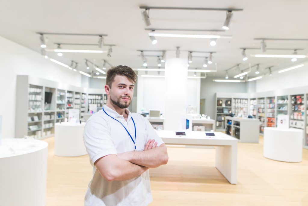 Smiling is a consultant on the background of modern light technology store. Portrait of a handsome man seller in an electronics store.