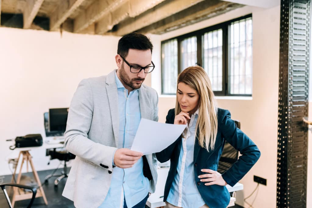 Two business people analyzing strategy of their work on paper documents while standing in office