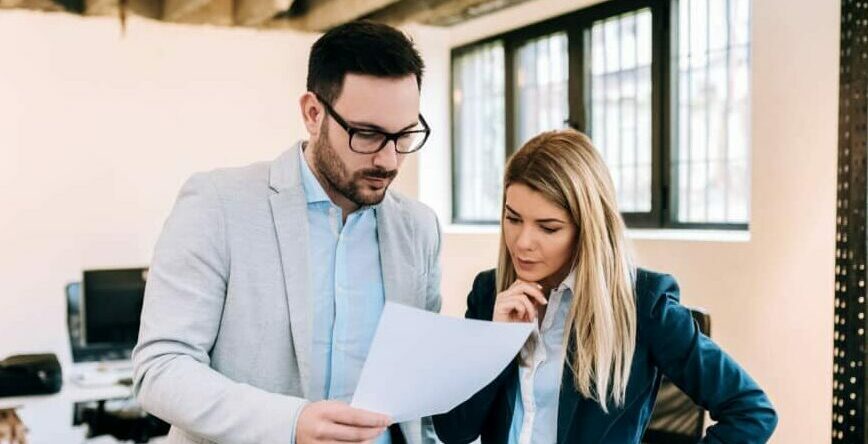 Two business people analyzing strategy of their work on paper documents while standing in office