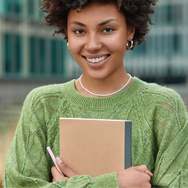 vertical-shot-happy-young-woman-with-curly-hair-holds-notepad-pen-makes-notes-what-she-observes-around-city-dressed-casual-green-jumper-poses-outdoors-against-blurred-background 1