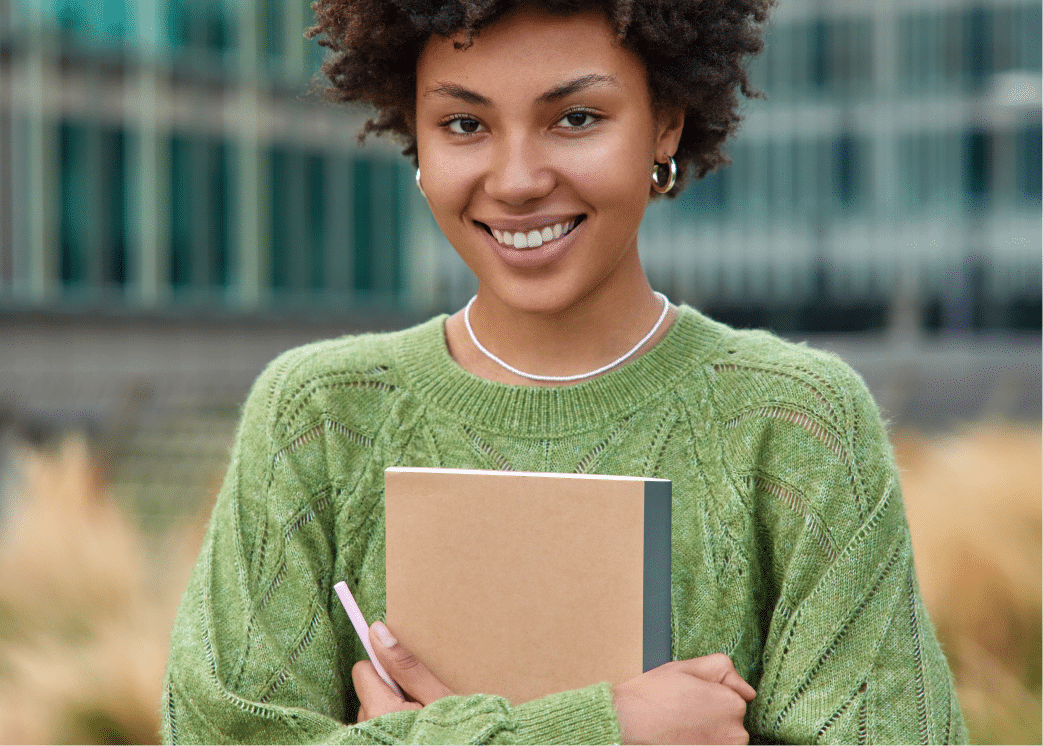vertical-shot-happy-young-woman-with-curly-hair-holds-notepad-pen-makes-notes-what-she-observes-around-city-dressed-casual-green-jumper-poses-outdoors-against-blurred-background 1